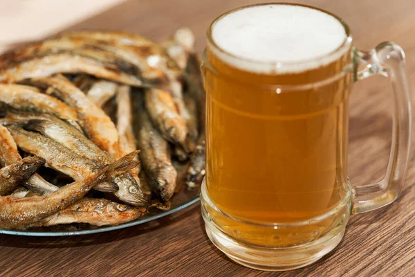 Bicchiere di birra e un piatto con piccolo pesce fritto profumato sul tavolo — Foto Stock