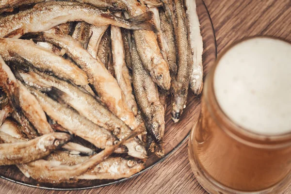 Склянка пива і тарілка з дрібною смаженою рибою, що розтанула на столі — стокове фото