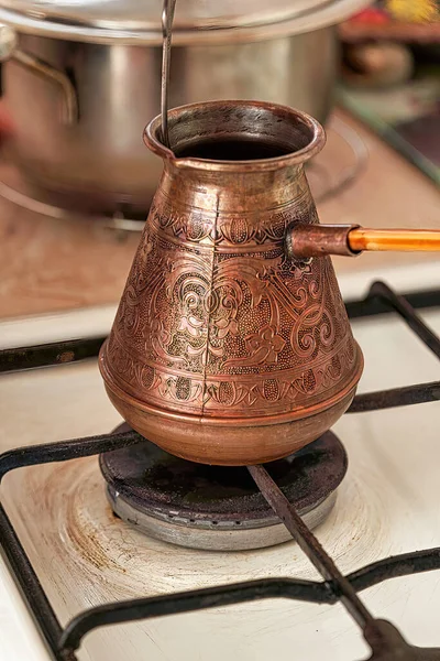 Cooking black coffee in a copper cezve on a gas stove in the kitchen at home. Close up