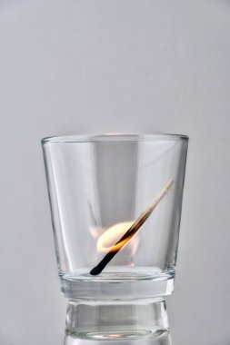 Işık arkaplanındaki şeffaf bir camda yanan kibrit