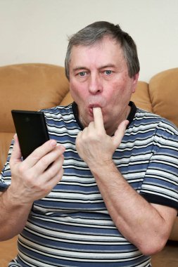 Bir adam koltukta otururken duygusal olarak akıllı telefona bakar. Haberlerdeki duygular.