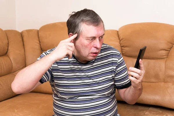 소파에 남자가 감정적으로 스마트폰을 들여다보고 있습니다 뉴스에서 나오는 감정들 — 스톡 사진