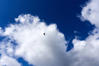 Bulutlu mavi gökyüzüne karşı bir helikopter silueti. Güneşli bir günde helikopter uçuşu