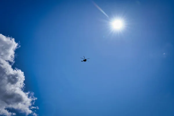 Silhouette of a helicopter against a blue sky with clouds. Helicopter flight on a sunny day