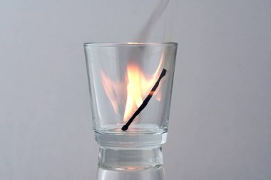 Hafif bir arkaplanda şeffaf bir bardakta ölen bir kibritin kalıntıları.