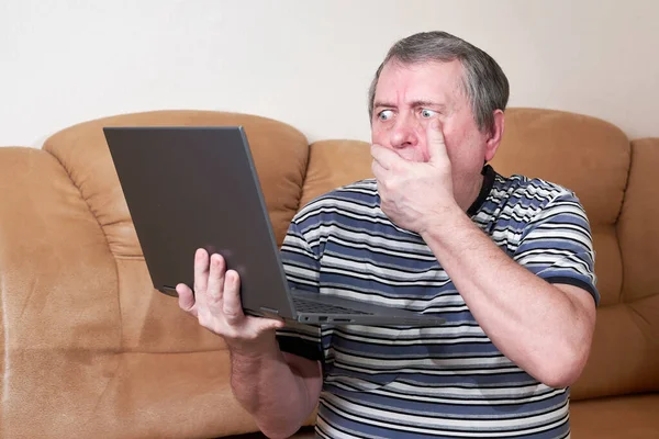 Человек с удивленным лицом держит ноутбук в руках, сидя на диване — стоковое фото