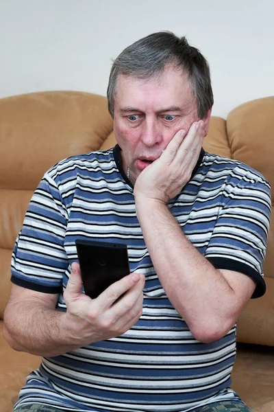 Мужчина смотрит эмоционально в смартфон, сидя на диване — стоковое фото