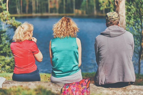 一个男人和两个女人坐在森林湖畔 — 图库照片