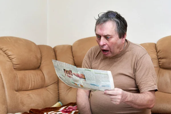 소파에 앉아 있는 나이든 남자가 신문에서 뉴스를 읽고 있어요. — 스톡 사진