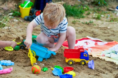 Küçük çocuk kumda plastik oyuncaklarla oynuyor. Kum havuzunda oynayan çocuk