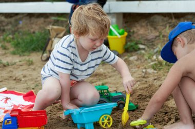 İki çocuk plastik oyuncaklarla kumda oynuyor. Kum havuzunda oynayan çocuklar