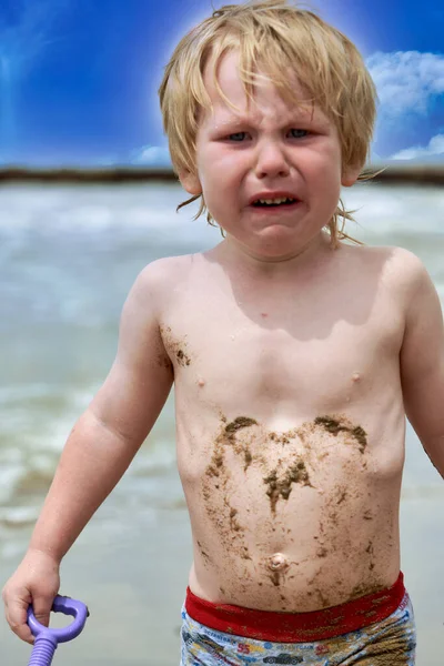 小さな男の子が泥の中で汚れて海に沿ってビーチに泣いて歩く — ストック写真