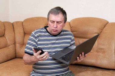 Şaşırmış suratlı bir adam koltukta otururken elinde dizüstü bilgisayar tutuyor. Haberlerdeki duygular.