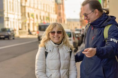 At kuyruklu uzun boylu bir adam sokakta bir kadınla konuşuyor. Bahar güneşli gün