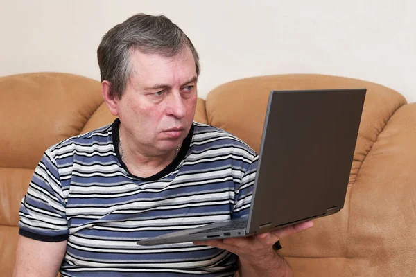 Человек с удивленным лицом держит ноутбук в руках, сидя на диване — стоковое фото