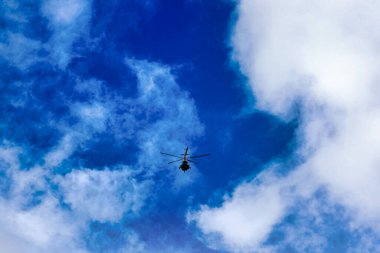 Bulutların ve mavi gökyüzünün üzerinde uçan helikopter