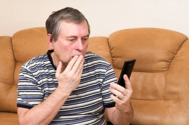 Bir adam koltukta otururken duygusal olarak akıllı telefona bakar.