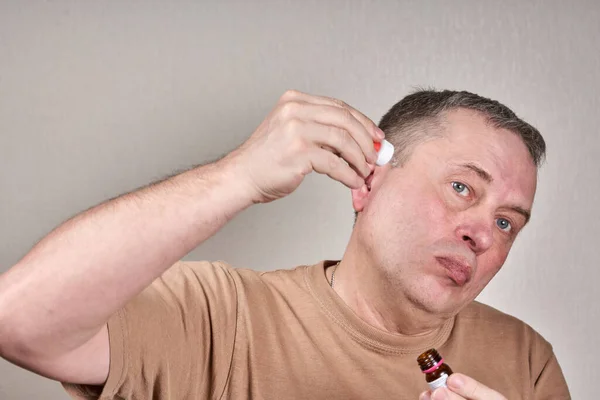 A man instills medicine into his ear with a small pipette from a pharmacy bottle