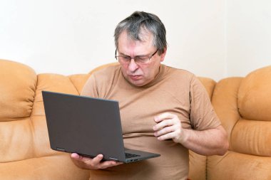 Devani 'nin üzerinde oturacak yaşta bir adam haberlere dizüstü bilgisayarla bakıyor..