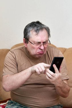 Kanepede oturan yaşlı vatandaş aleti anlıyor, akıllı telefonda ustalaşıyor.