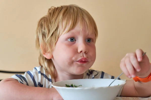 Un petit garçon avec une bouche sale mange avec une cuillère d'une assiette — Photo