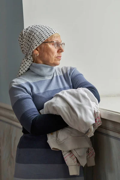 一个头戴围巾戴眼镜的女人的画像靠在窗台上 老妇人站在窗边 — 图库照片