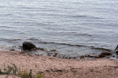 Gölün kıyısında kumlu bir sahil ve suda bir taş var. Doğal manzara.