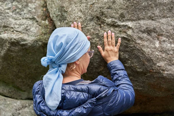 A woman with a scarf on her head touches a stone with her hands. Religious pilgrims take strength from a stone