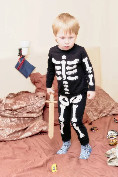 Een kind in een skelet kostuum met een houten zwaard speelt op de bank — Stockfoto