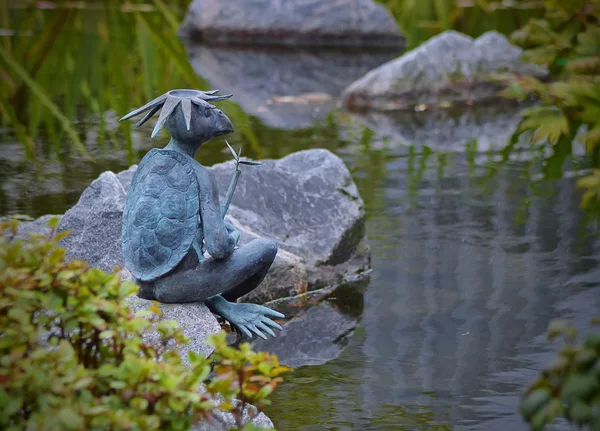 Bronze sculpture kappa seated on a stone by the pond. — Stock Photo, Image