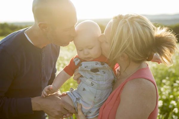 Heureuse famille de trois personnes. Père, mère et bébé jouant dehors en été au coucher du soleil . — Photo