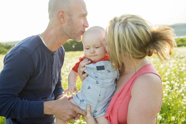 Heureuse famille de trois personnes. Père, mère et bébé jouant dehors en été au coucher du soleil . — Photo