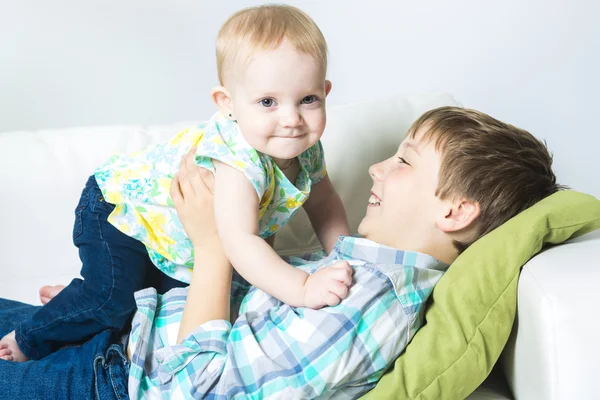 Lycklig pojke håller hans syster baby på soffa — Stockfoto