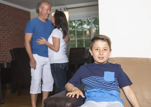 Menino sentado no sofá em casa, pais no fundo — Fotografia de Stock