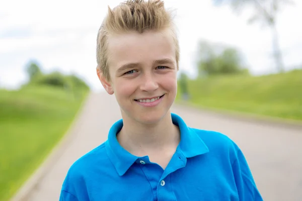 Young happy smiling male boy teenager blond child outside in summer sunshine wearing a blue sweatshirt — Stock Photo, Image