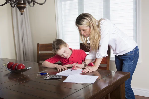 Мать за столом дома помогает своему маленькому сыну с домашним заданием — стоковое фото