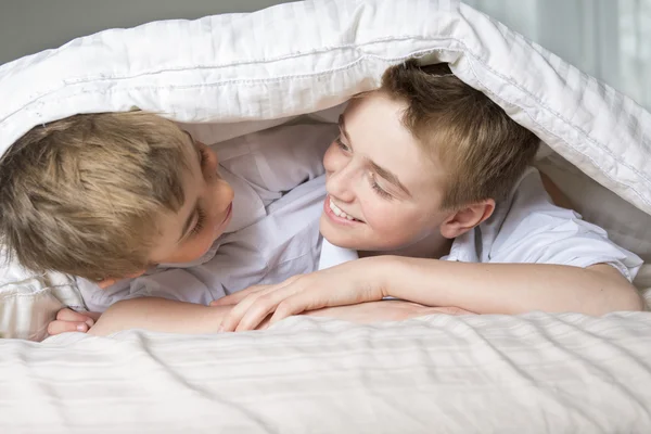 Menino escondido na cama sob um cobertor branco ou coverlet . — Fotografia de Stock