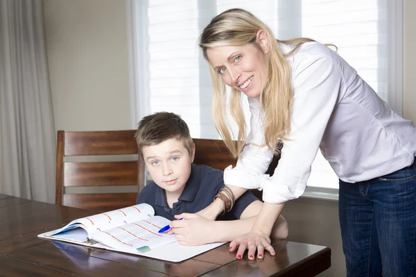 그의 숙제와 그녀의 작은 아들을 돕는 홈 테이블에 어머니 — 스톡 사진