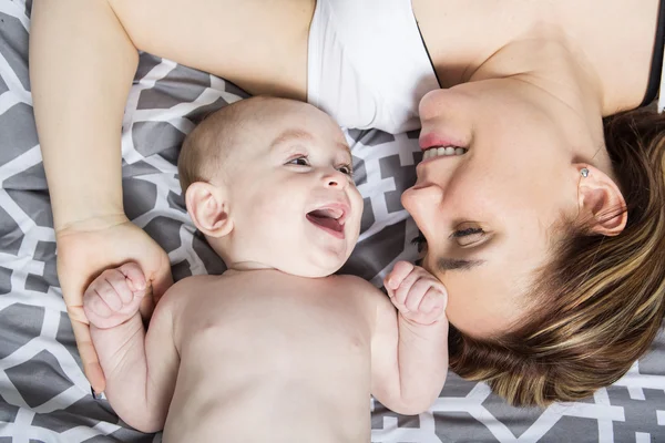 Retrato de madre joven y feliz con un bebé en la cama en casa — Foto de Stock