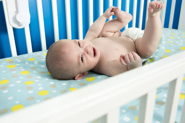 Cute one month old newborn baby is laying on her back in the crib, crying. — Stock Photo, Image