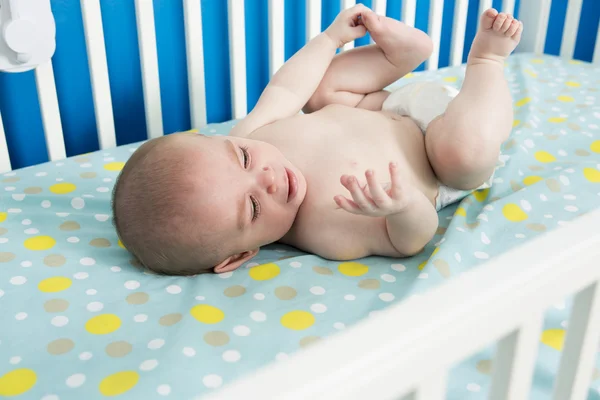 Cute one month old newborn baby is laying on her back in the crib, crying. — Stock Photo, Image