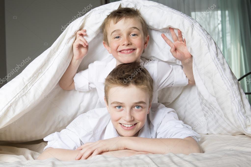 Boy hiding in bed under a white blanket or coverlet. — Stock Photo