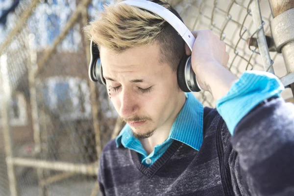 Stilig man lyssna på musik med hörlurar nära stängslet utomhus. — Stockfoto