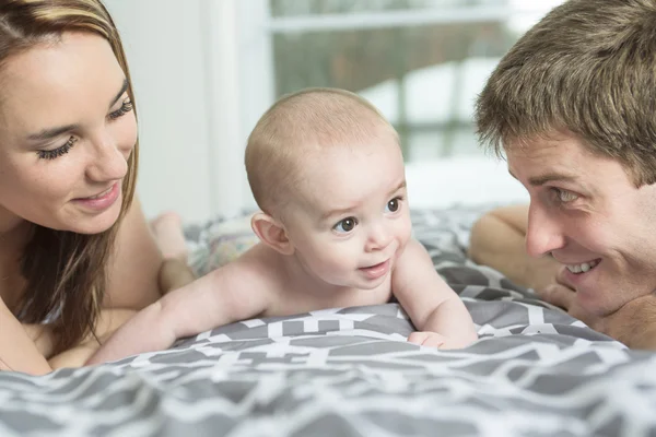 Famille heureuse de père, mère et bébé jouant au lit — Photo