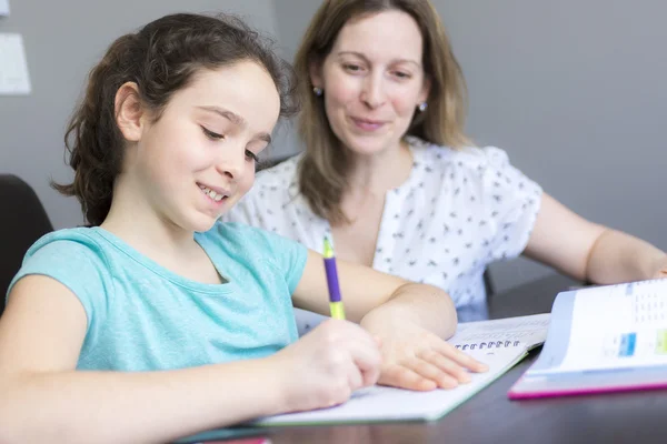 Зріла мати допомагає своїй дитині з домашнім завданням вдома . — стокове фото