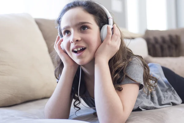 Donna che ascolta musica in cuffia sul divano in camera — Foto Stock