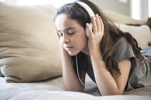 Vrouw luisteren muziek in hoofdtelefoons op sofa in kamer — Stockfoto