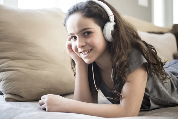 Vrouw luisteren muziek in hoofdtelefoons op sofa in kamer — Stockfoto