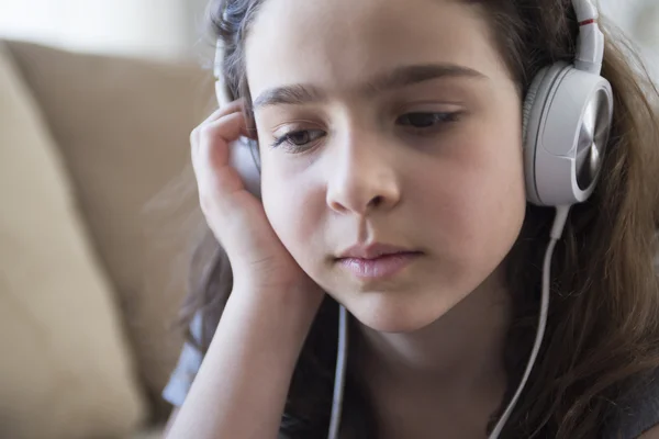 Vrouw luisteren muziek in hoofdtelefoons op sofa in kamer — Stockfoto