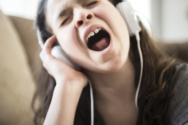 Žena poslech hudby ve sluchátkách na pohovce v místnosti — Stock fotografie